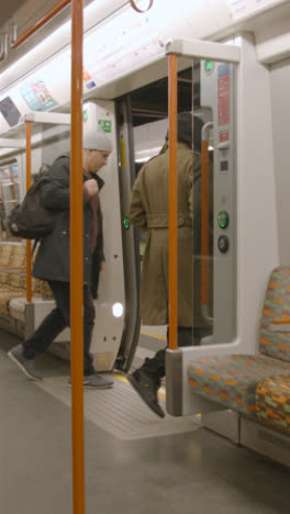 Vertical-Video-Interior-Shot-Of-Commuter-Passengers-Getting-Off-UK-Train-At-Station